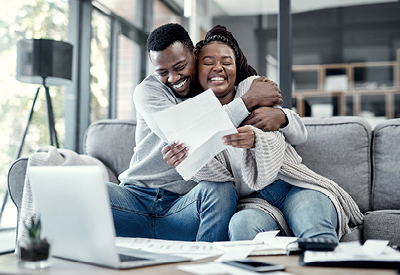 Young African-Amarican couple smiling and embracing on sofa while looking at financial statements