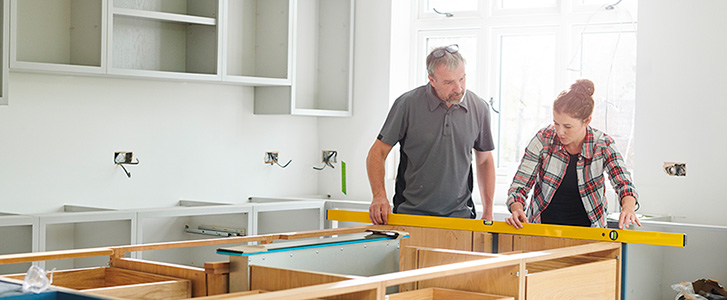 Two people using a level on a kitchen island.