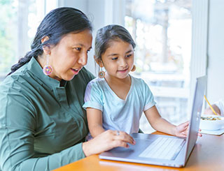 Mom and daughter using a laptop to shop Trustmark accounts.