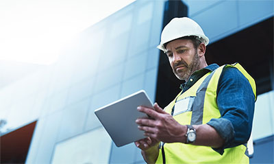 Man wearing hardhat and looking at tablet computer.