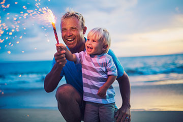 Father and young son using fireworks on beach.