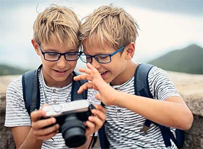 Two boys with blue glasses looking at SLR camera.