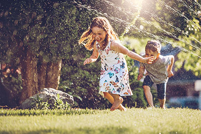Two children playing in sprinklers.