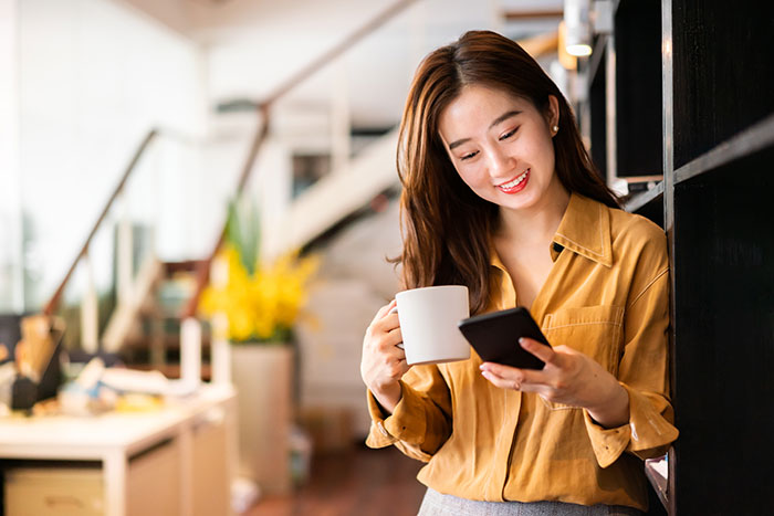 Young lady holding coffee cup and looking at a smartphone.