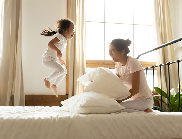 Mom laughing while daughter jumps on bed.